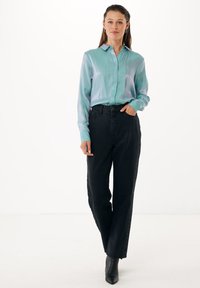 Lichtgroene satijnen blouse met lange mouwen en kraag, gecombineerd met hoog-waist zwarte denim broek met zijknopen en zakken.