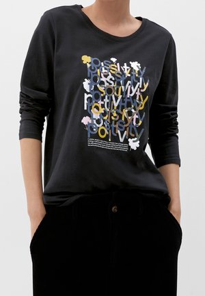 Persona con una camiseta de manga larga negra con letras superpuestas multicolores y pequeñas formas florales en la parte delantera.