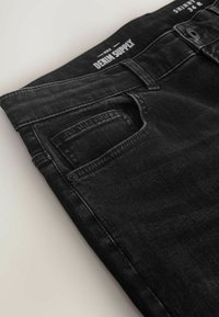 Jeans negri din denim, cu croială skinny, talie clasică și un buzunar frontal. Deteriorările subtile de pe țesătură îmbunătățesc textura.