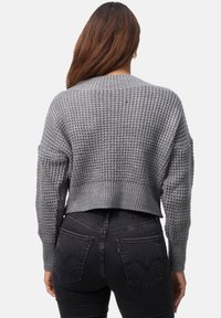 Grå stickad tröja med ett strukturerat mönster, kort design och vida ärmar, parat med högmidjade svarta jeans med bakfickor.