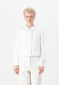 Jachetă din denim albă, scurtă, cu guler clasic, două buzunare frontale și închidere cu nasturi. Textură netedă cu detalii franjurate la tiv.
