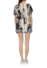 Zwart en crèmekleurig tie-dye shirt, korte mouwen, losse pasvorm, afgeronde zoom, achterkant met splitdetail. Gepaard met denim shorts en zilveren sneakers.