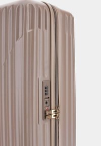 Hard-shell suitcase in beige, featuring textured ribbed design, gold-tone hardware, zipper closure, and a built-in combination lock.