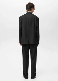 Completo nero su misura con blazer strutturato e pantaloni dritti, caratterizzato da un tessuto liscio e un design minimalista. Vista dal retro.