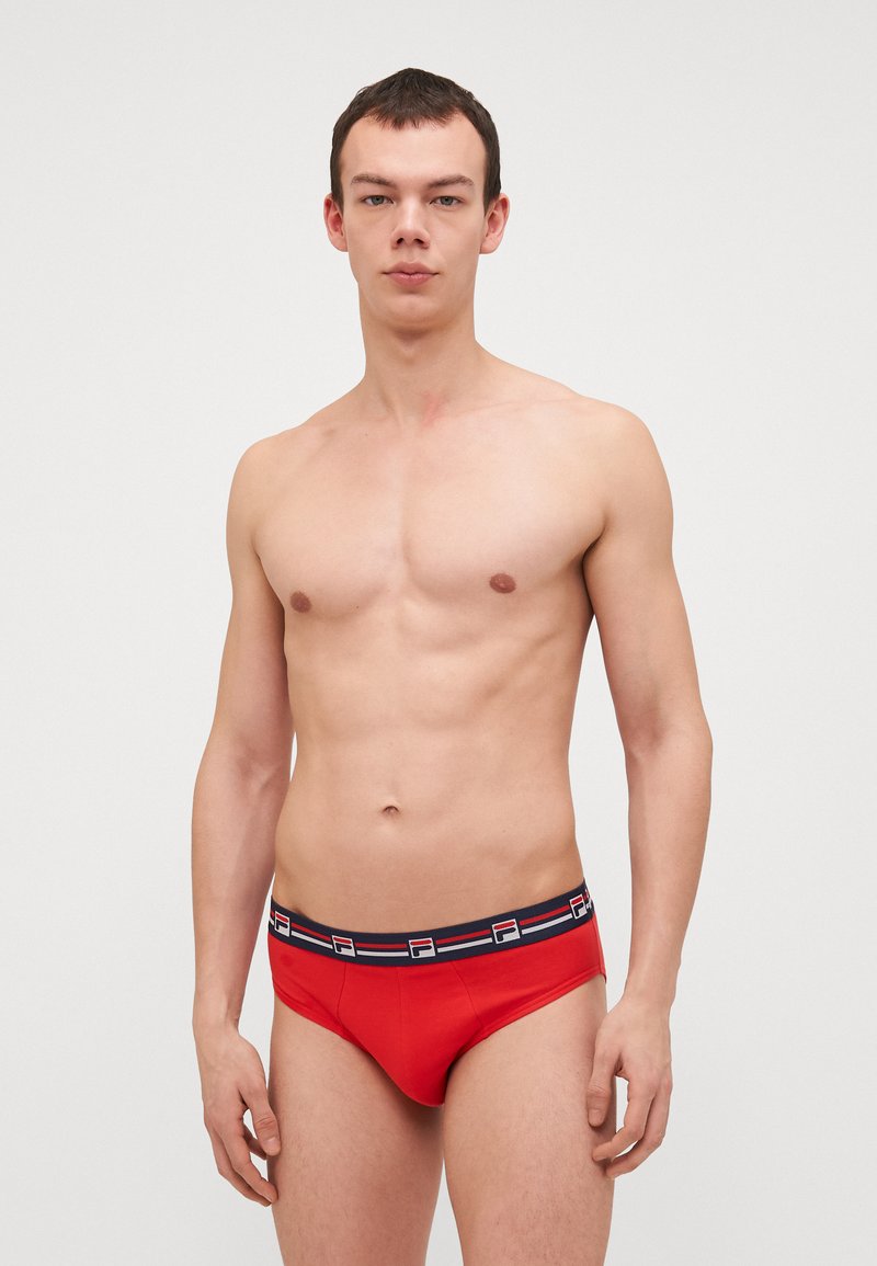Slip rossi con una vita a contrasto nera, decorata con un logo e strisce multicolori. Tessuto liscio, design aderente e leggero lucido.