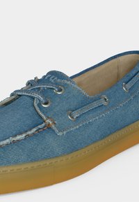 Μπλε τζιν παπούτσι τύπου μοκασίνι με μπεζ εσωτερικό, καφέ ραφές, μεταλλικά οπές, κορδόνια και ανοιχτό καφέ λαστιχένια σόλα.