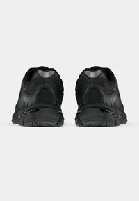 Fekete sportcipők texturált felsőrésszel, párnázott talppal és jellegzetes sarokdizájnnal. Megerősített elemek a hátsó és oldalsó részeken.