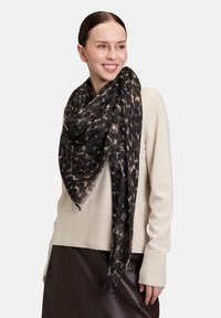 Schwarz-beige Leopardenmuster-Schal aus weichem, leichtem Stoff; mit fransigen Kanten und locker um den Hals drapiert.