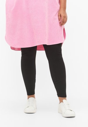 Mustat legginsit yhdistetty vaaleanpunaiseen pitkään tunikapaitaan. Legginsit ovat tiukat ja joustavat, kun taas tunikassa on sileä, teksturoitu pinta.