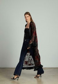 Kimono negru și burgund cu motive florale și margini ciufulite, purtat cu un top negru și blugi evazați de un albastru închis. Sandale cu toc.