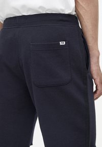 Pantaloni della tuta blu navy realizzati in tessuto morbido, dotati di una tasca posteriore con etichetta, righe laterali e una vita elastica.