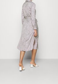 Dlouhé šaty se vzorem zebry v světle šedé a bílé barvě, s dlouhými rukávy, zavazováním v pase, bočními rozparky a volným střihem. Nošeny s bílými sandály na podpatku ve tvaru bloků.