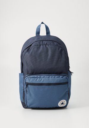 Zaino blu navy con una tasca frontale azzurro chiaro, dotato di chiusura con zip, tessuto testurizzato e una toppa rotonda con il logo di Converse.