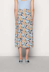 Saia midi floral com um fundo preto, featuring flores laranja e azuis. Cintura elástica e tecido fluido, combinada com mules de salto azul claro.