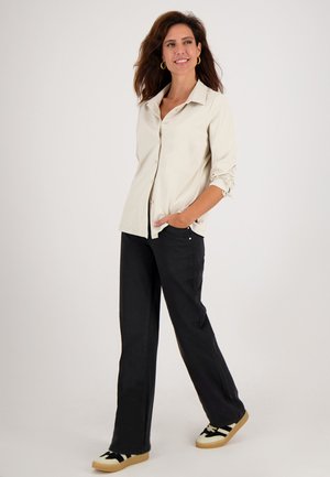Beige button-down overhemd met lange mouwen, gecombineerd met zwarte wijde broek en zwart-witte sneakers met een patroon. Gladde stoftextuur.