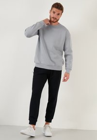 Sudadera gris claro con cuello redondo, puños y dobladillo acanalados. Combinada con pantalones jogger negros y zapatillas blancas.
