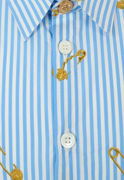 Chemise à rayures bleues et blanches avec un imprimé novateur doré de épingles de sécurité et de fil. Elle présente un col pointu et des boutons standards. Texture en coton doux.