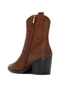 Bota de cowboy de cuero marrón con un patrón decorativo de costura, cremallera lateral y un tacón grueso y texturizado en negro. Acabado sintético de alta calidad.