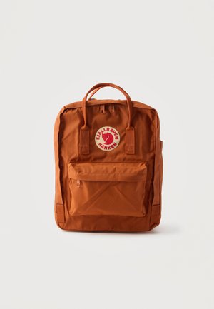 Sac à dos Fjällräven Kånken couleur rouille avec poche avant zippée, poignées supérieures et écusson rond avec logo sur fond blanc uni.