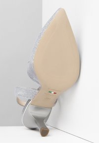 Chaussure à talons aiguilles argentée avec une tige texturée, bout ouvert et brides transparentes. Talon courbé et semelle beige avec le logo de la marque et la taille 37 imprimés.