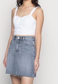 Woman wearing a white cropped tank top and a high-waisted, faded blue denim mini skirt with raw hem detailing.