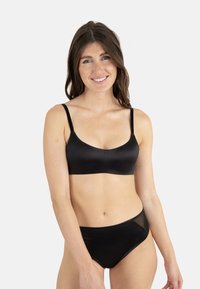 Bralette noire avec des bretelles fines, en tissu doux et au design sans couture. Bas de bikini noir assorti avec des accents de panneaux latéraux transparents.