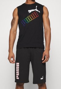 Canotta nera senza maniche con logo "PUMA" multicolore e grafica di un gatto bianco; abbinata a pantaloni corti neri con testo "PUMA" in rosa.