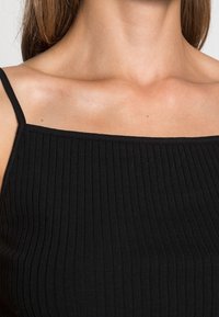 Svart ribbad linne med tunna axelremmar och fyrkantig halsringning, som framhäver ett texturerat tyg och en åtsittande design.