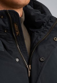 Temno modra jakna z vloženo teksturo, ki ima izrazit zadrgo in zapiranje na pritiskače, ter oznako z napisom "PME LEGEND AMERICAN CLASSIC."