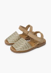 Geweven gouden en tan sandalen met een gestructureerde voorband, suede-achtige materiaal en verstelbare achterriem; rubberen zool voor grip en comfort.