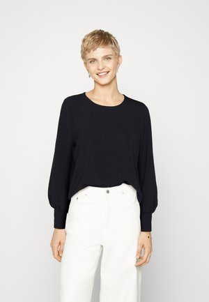 Haut noir à manches longues avec un col rond et une coupe ample, associé à un pantalon large blanc. Texture lisse ; design décontracté ; sans motifs.