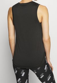 Haut de sport noir sans manches avec encolure ronde, en tissu lisse ; associé à des leggings noirs ornés d'un texte de marque blanc.