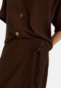 Brązowy zestaw z fakturą, składający się z koszuli z krótkim rękawem zapinanej na złote guziki oraz spodenek o luźnym kroju z zawiązywanym sznurkiem w pasie.