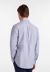 Camicia button-up a righe celesti con maniche lunghe, colletto classico e dettaglio della spallina sul retro. Il tessuto appare liscio e tessuto.