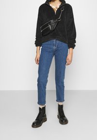 Sudadera de forro polar negra con cremallera de cuarto, vaqueros de mezclilla azul y botas de combate negras con cordones. Accesorio: pequeña bolsa negra de cintura con cadena.