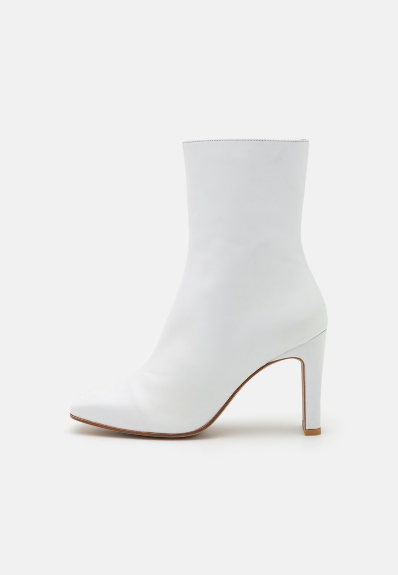 Bottine en cuir blanc à bout pointu, avec un talon aiguille haut et une texture lisse. Design minimaliste sans hardware ni accents visibles.