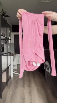 Maglietta rosa a maniche lunghe realizzata in tessuto morbido, con scollo rotondo, dettagli arricciati al collo e orlo drappeggiato con spacchi laterali.