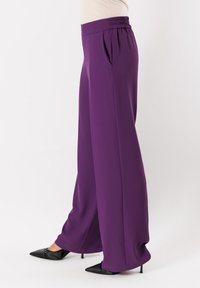 Pantaloni larghi viola realizzati in tessuto morbido, con vita elastica arricciata e tasche laterali, abbinati a décolleté nere a punta.