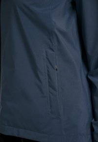 Veste imperméable bleu marine avec un design élégant, une texture lisse et une poche latérale équipée d'une fermeture éclair. Légère et fonctionnelle.