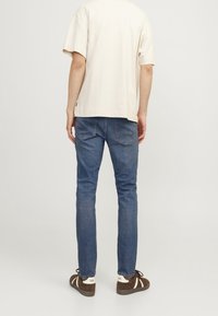 Camiseta de algodón beige de manga corta, combinada con jeans de mezclilla azul de corte slim y zapatillas marrones con acentos blancos.