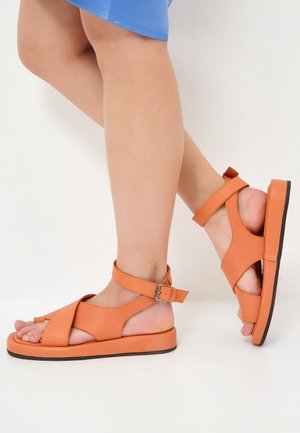 Open-toed sandalen van feloranje leer, met kruislingse banden, een gesp-sluiting en een dikke, platte zool. Gladde textuur.