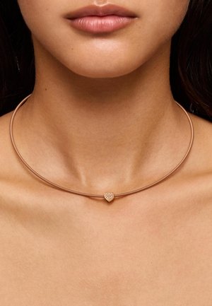 Collar choker en tono dorado con un diseño liso y delgado, que presenta un colgante en forma de corazón adornado con pequeños cristales en el centro.
