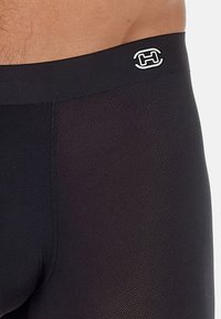 Black swim shorts with a textured pattern, featuring a logo on the waistband. Made from stretchy material, offering a fitted design.