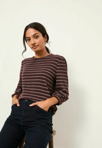 Burgunder gestreiftes Langarmoberteil mit grauen Streifen, Rundhalsausschnitt und eng anliegenden Ärmeln, kombiniert mit dunklen Jeans.