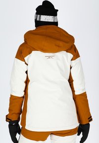 Giacca da sci con un design a blocchi di colore marrone e bianco, dotata di cappuccio, polsini regolabili e dettaglio del logo sulla schiena. Tessuto isolante.