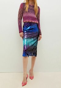 Fialová a modrá flitrová midi sukně spárovaná s texturovaným pleteným svetrem v červené a růžové barvě. Modelka má na sobě růžové lodičky s špičatou špičkou.
