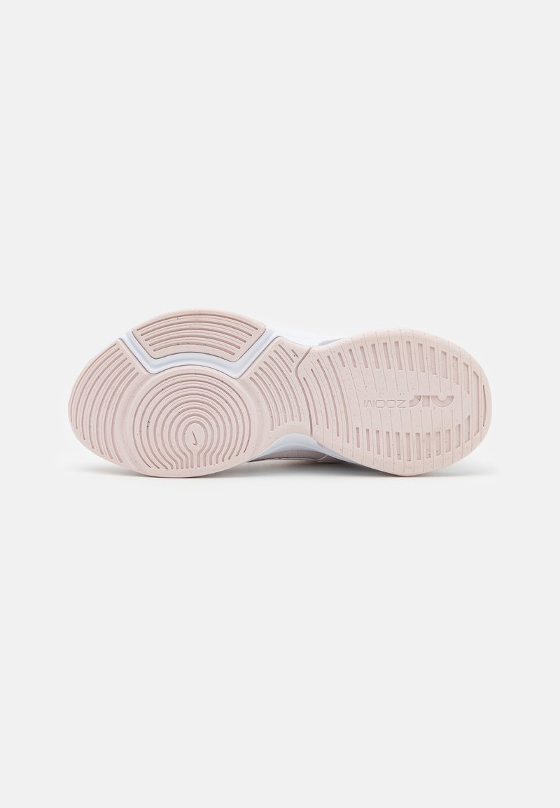 Semelle de chaussure avec un design en caoutchouc texturé de couleur rose pâle, présentant des motifs circulaires concentriques et des rainures pour une traction et une flexibilité optimales.