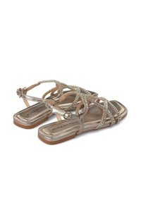 Sandali metallici argento con più cinghie incrociate, impreziositi da strass, e una suola piatta. Chiusura con fibbia sulla cinghia alla caviglia.