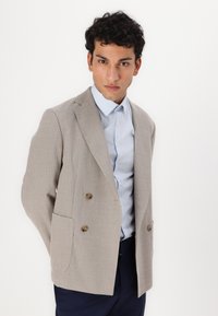 Beige stripete blazer med dobbeltradede knapper, to frontlommer, kombinert med en lyseblå stripete skjorte.