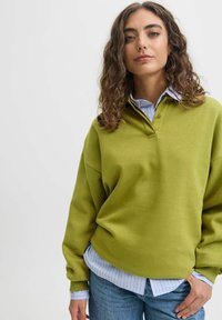 Olive green oversized sweatshirt with a collared neckline layered over a light blue and white striped shirt, paired with denim jeans.
